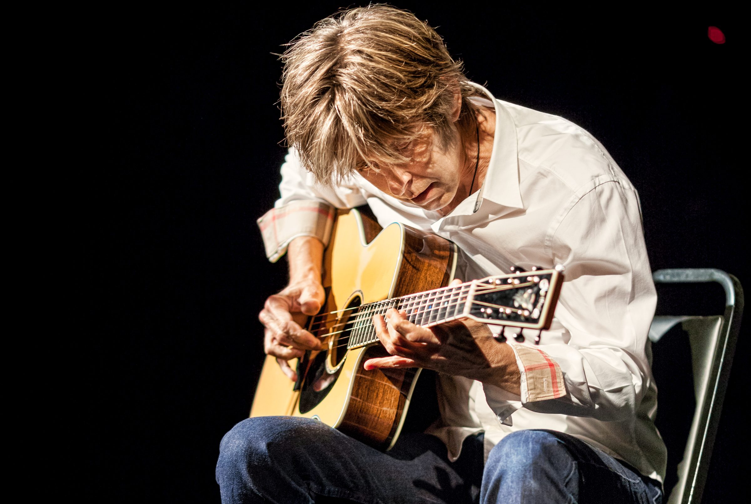 Eric Johson on stage, playing the guitar passionately.