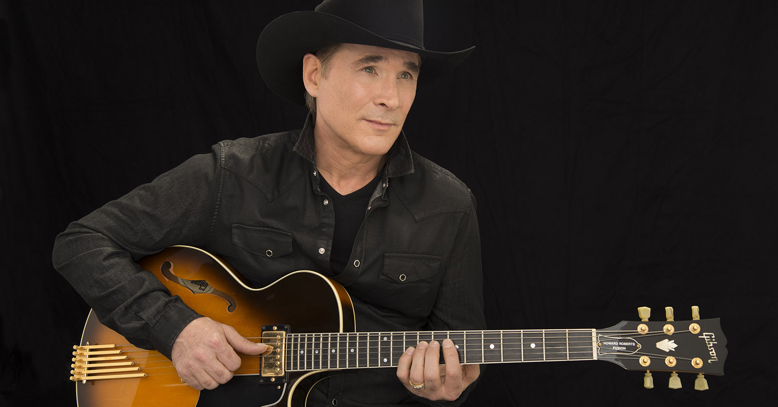 Clint Black holding a guitar and staring into the middle distance.