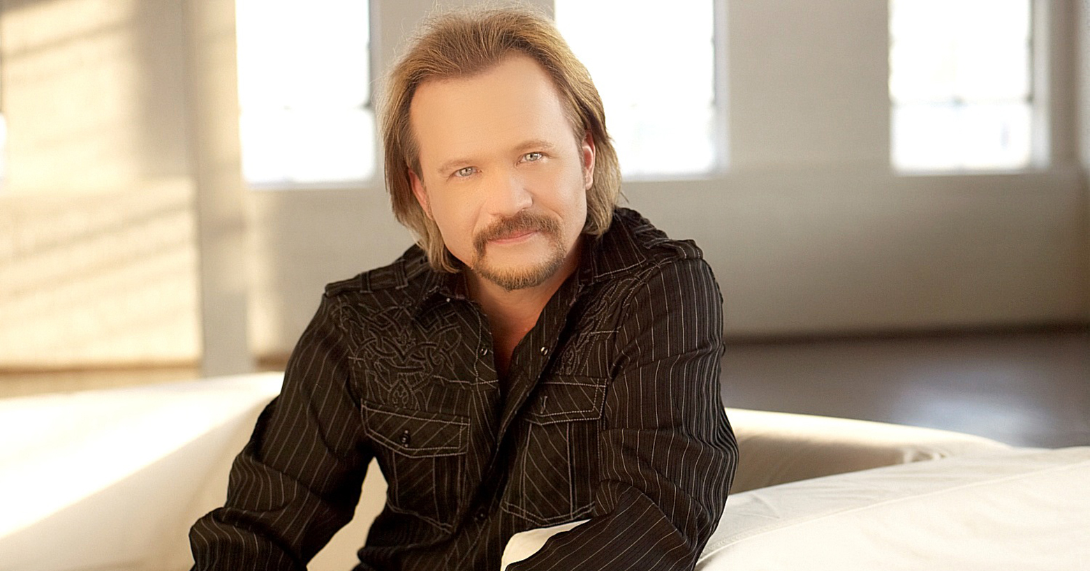 Travis Tritt staring at hte camera in a light, airy room.