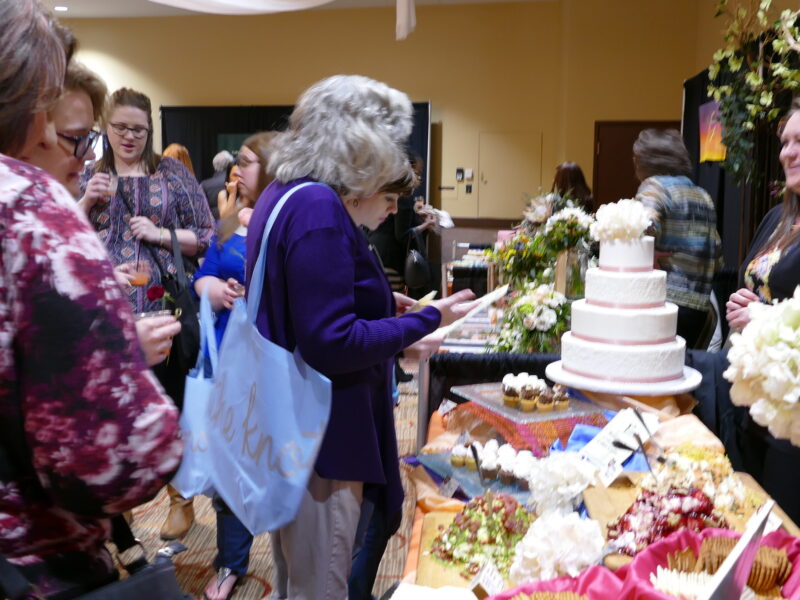 Wedding fair goers inspect a caterers table filled with goodies and cakes.