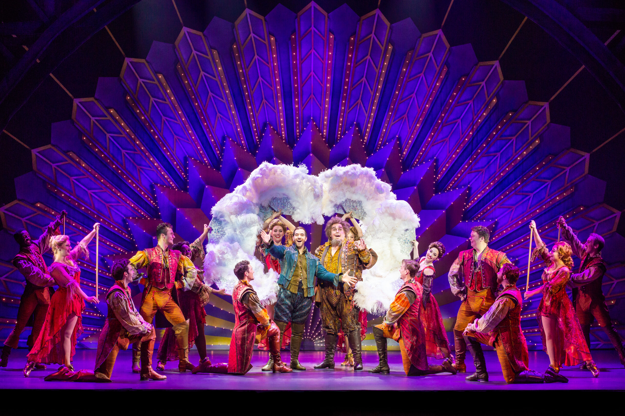 The cast of Something Rotten signing in front of a Las Vegas-style showgirl backdrop.