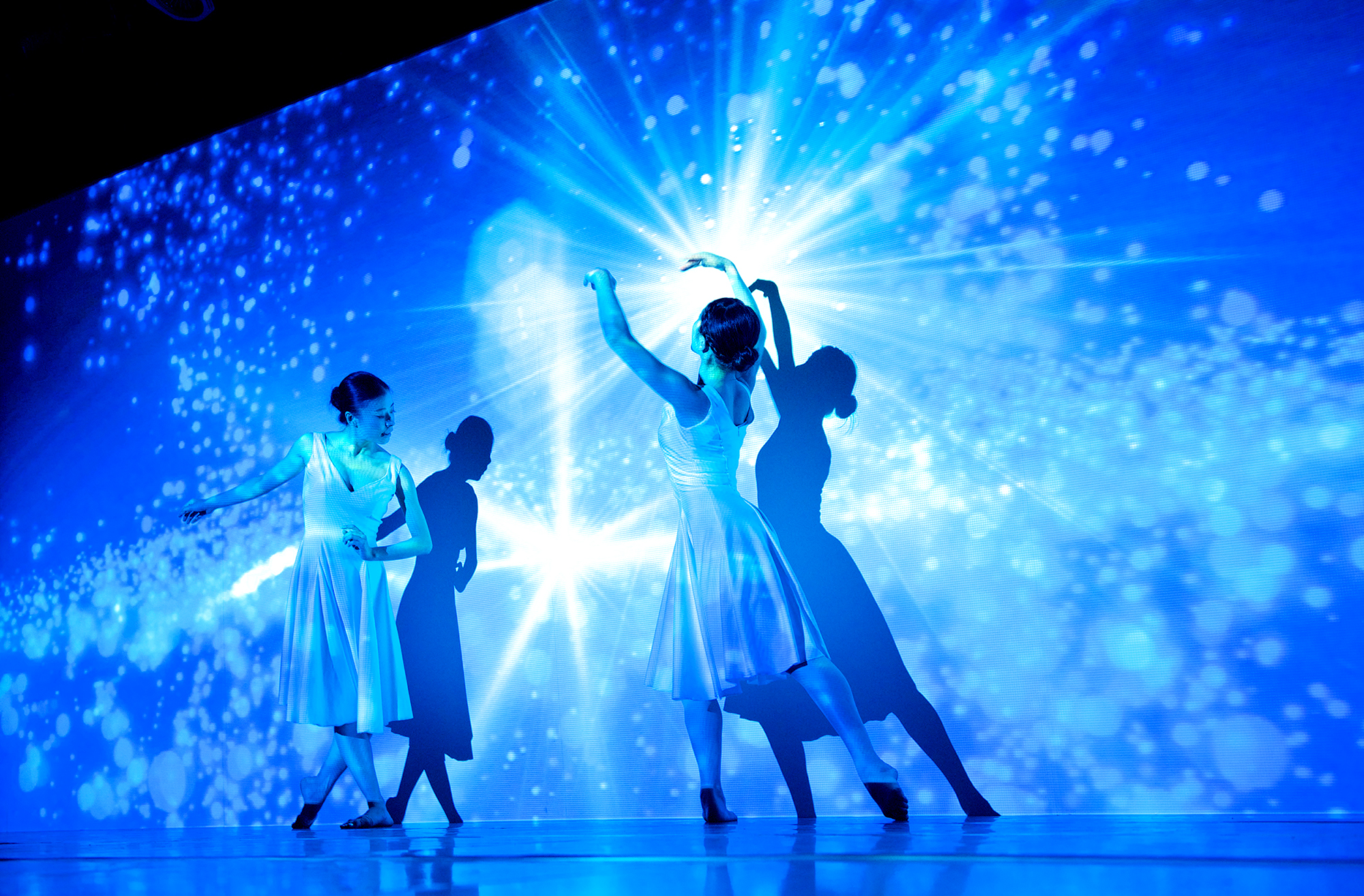Two dancers from enra playing with a light against a blue backdrop.