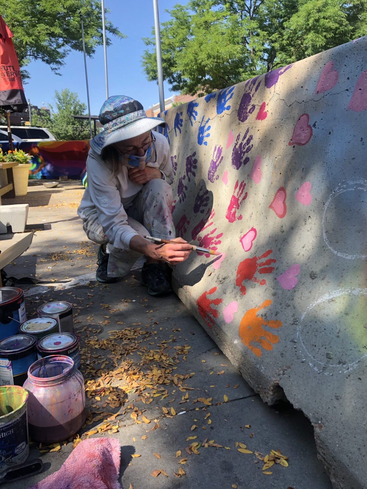 Gale Whitmana paiting a mural with colorful handprints on a concrete barrier.