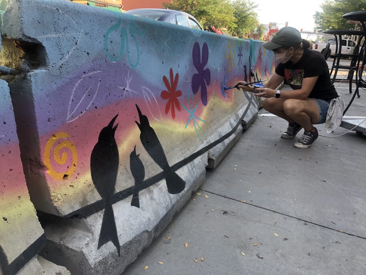 Ren Burke painting a mural of bird silhouettes on a dusky gradient.