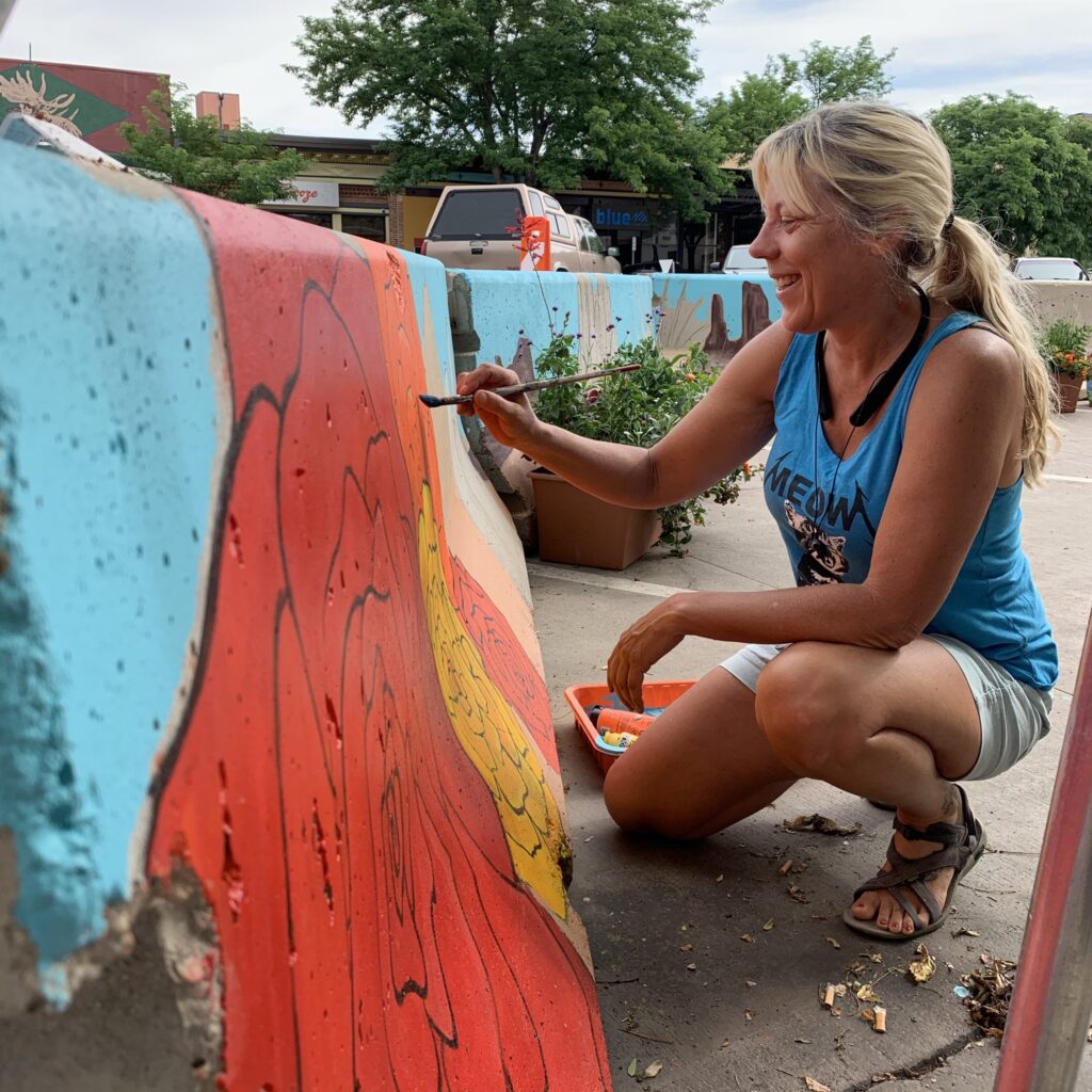 A woman painting a mural on a concrete barrier in downtown Fort Collins