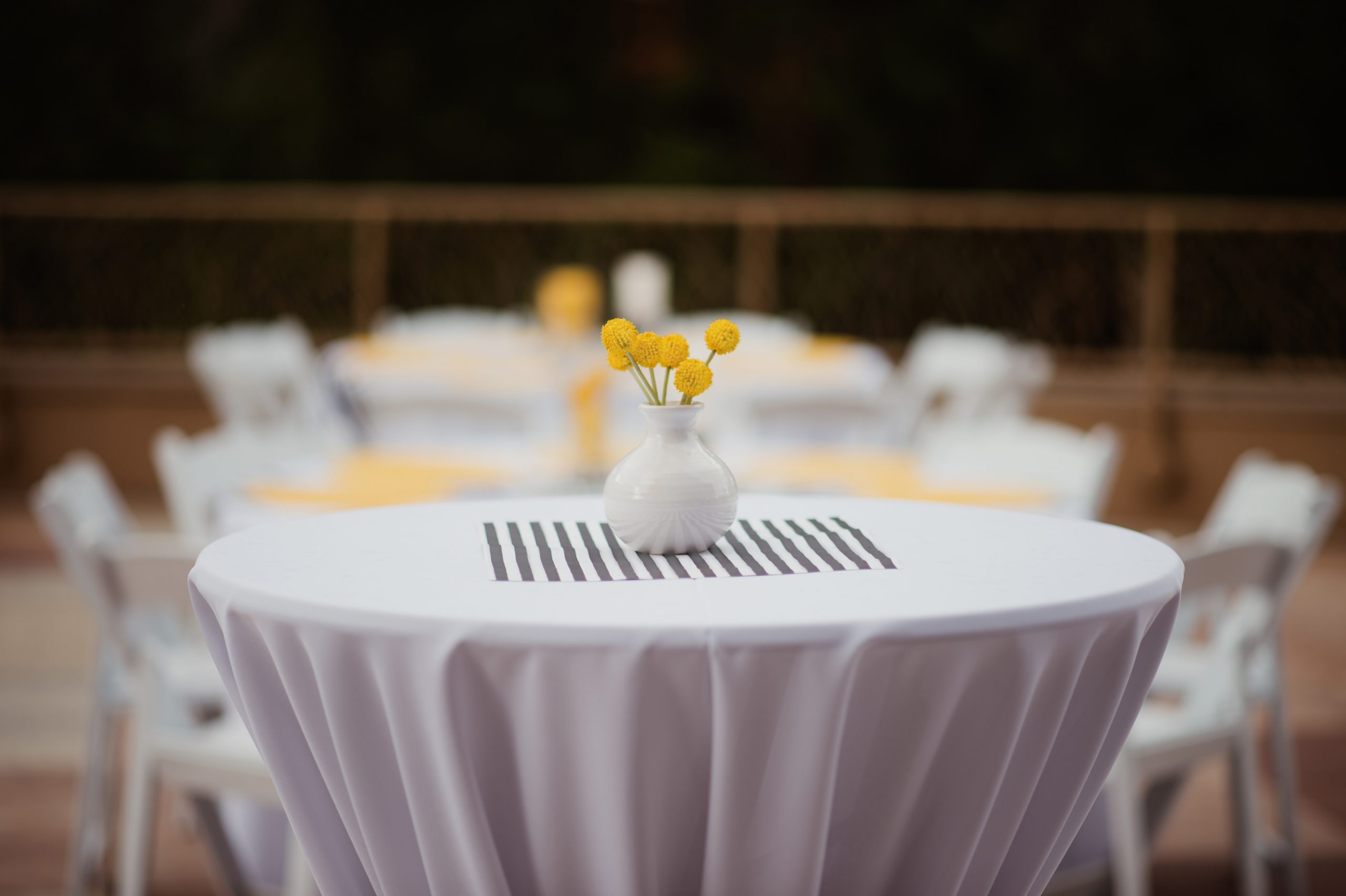 A white and black table setting with a bright yellow flower on the Rooftop Deck.