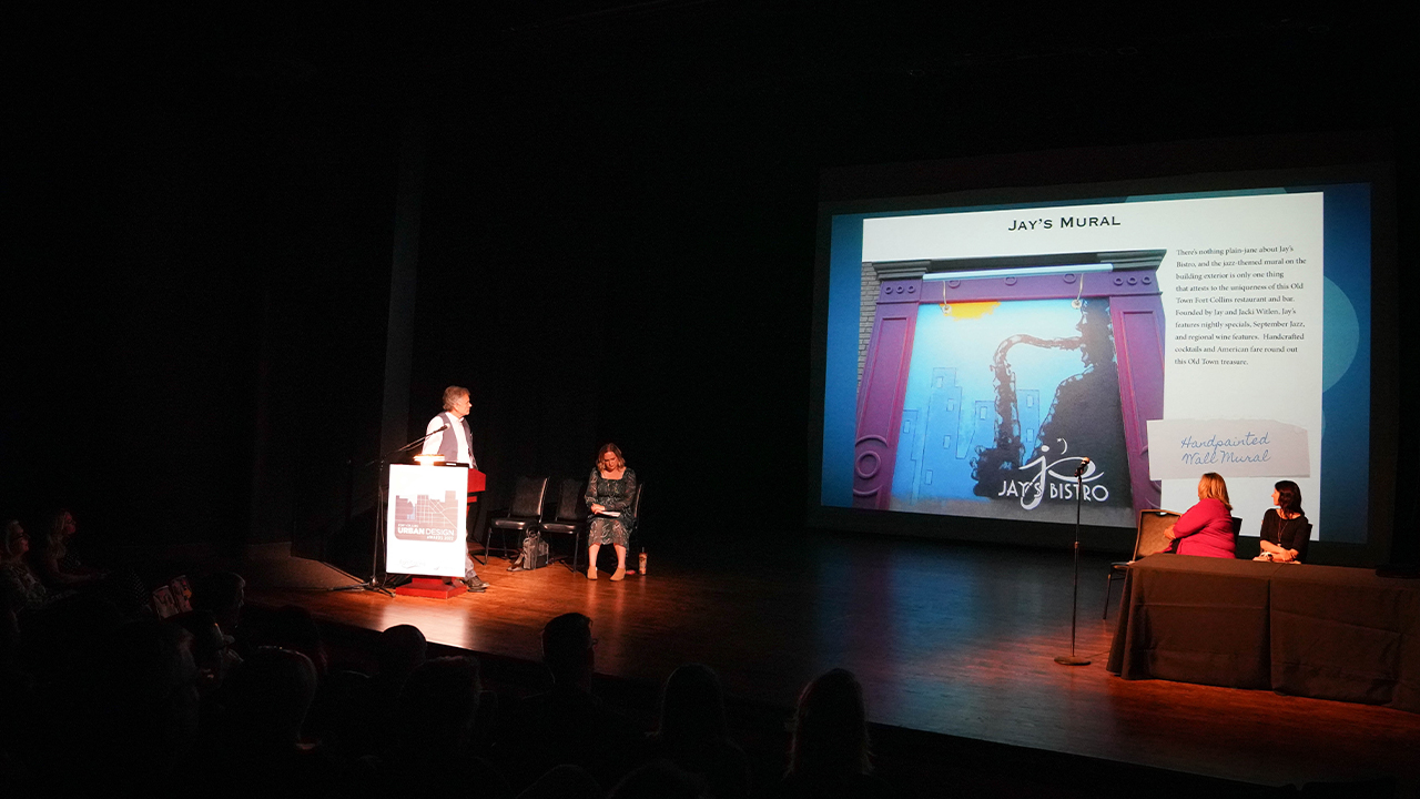 Presenters sit on Magnolia Theatre stage in front of a project screen.