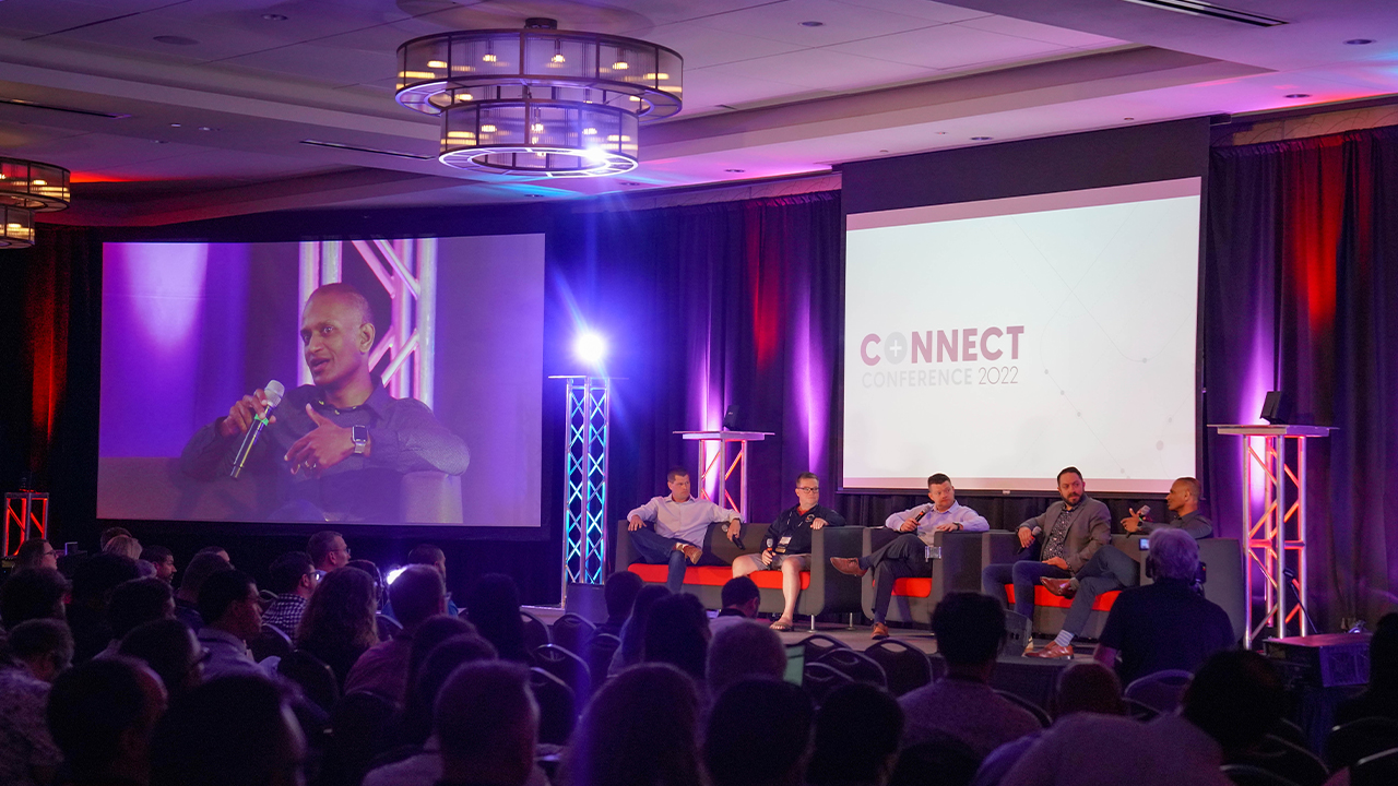 A panel of speakers sit on a stage in Canyon West Ballroom and present to convention attendees.