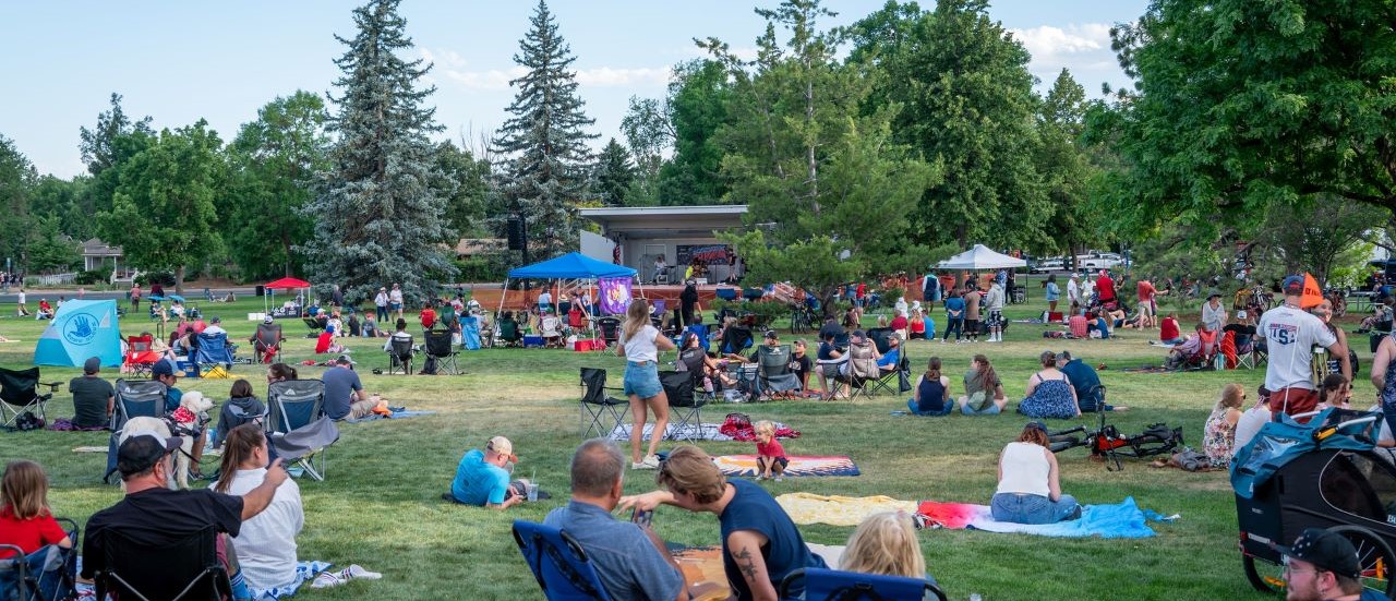 Groups of people sitting on picnic blankets facing an outdoor stage in City Park