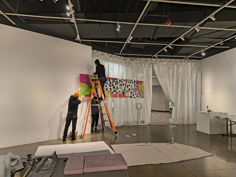 The Lincoln Center Art Gallery staff hanging an artwork featuring a butterfly.